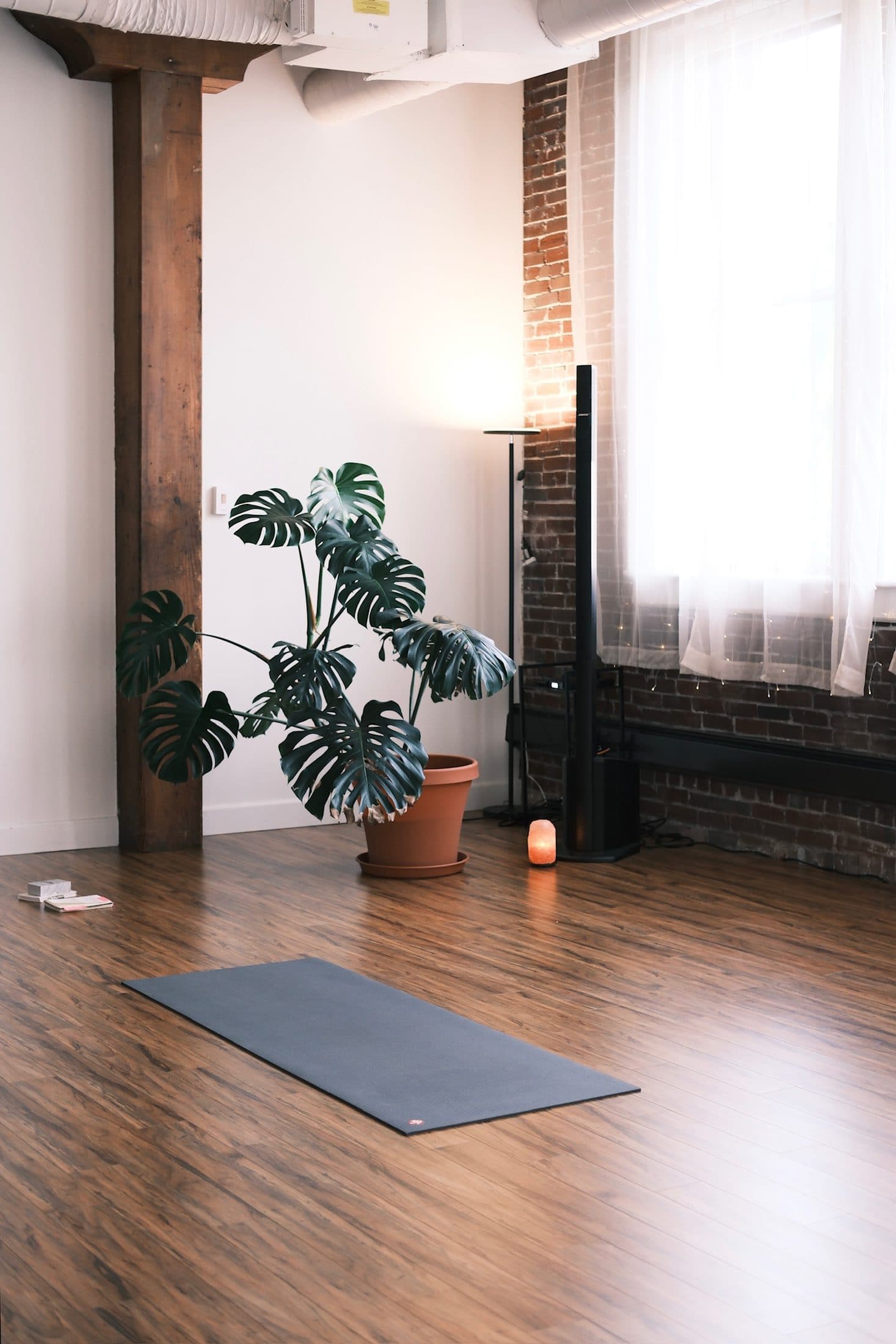Studio corner with a grey mat on warm wood floors, a monstera, and a timber post
