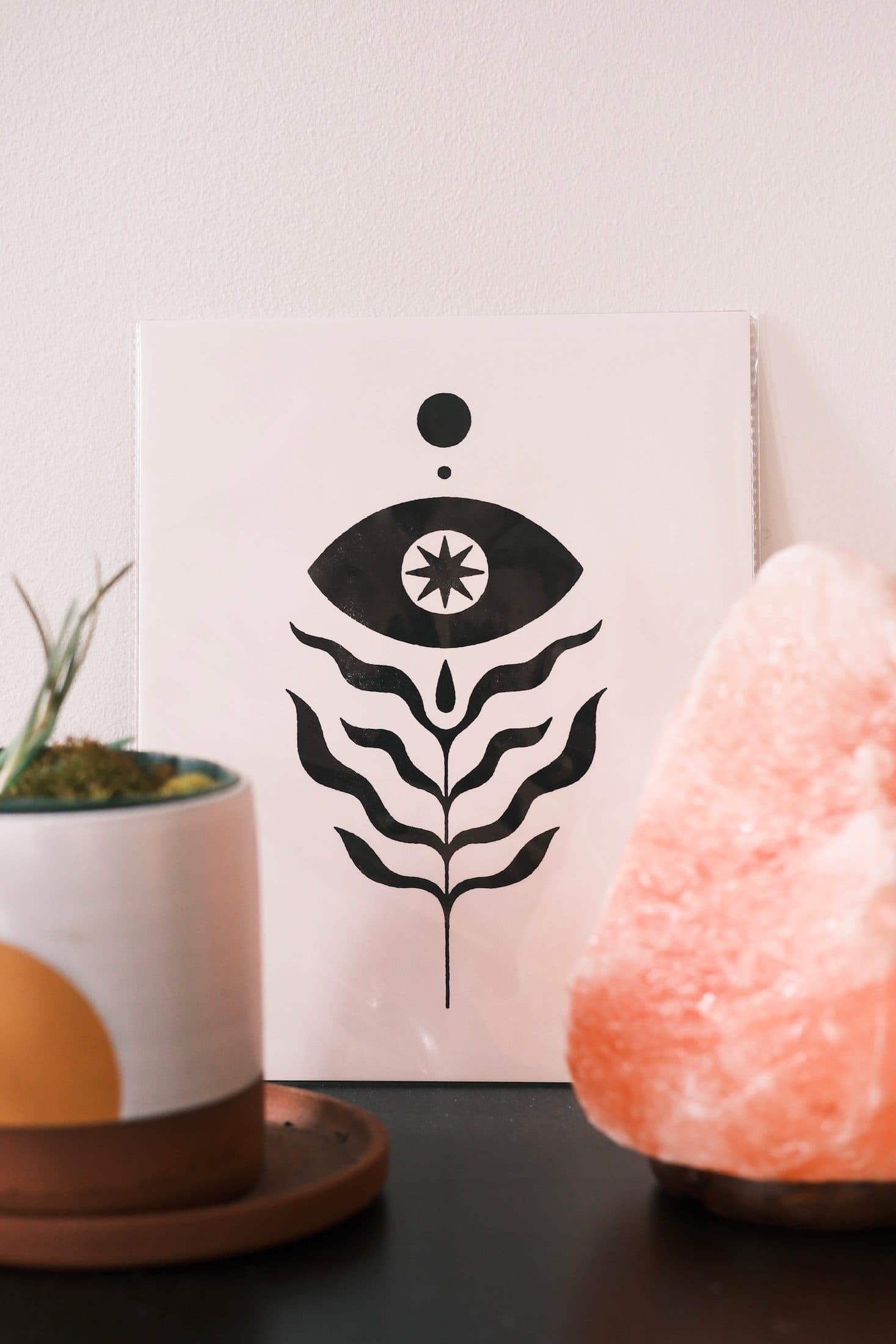 Salt lamp, planter, and a black-and-white print of an eye resting on a dark table