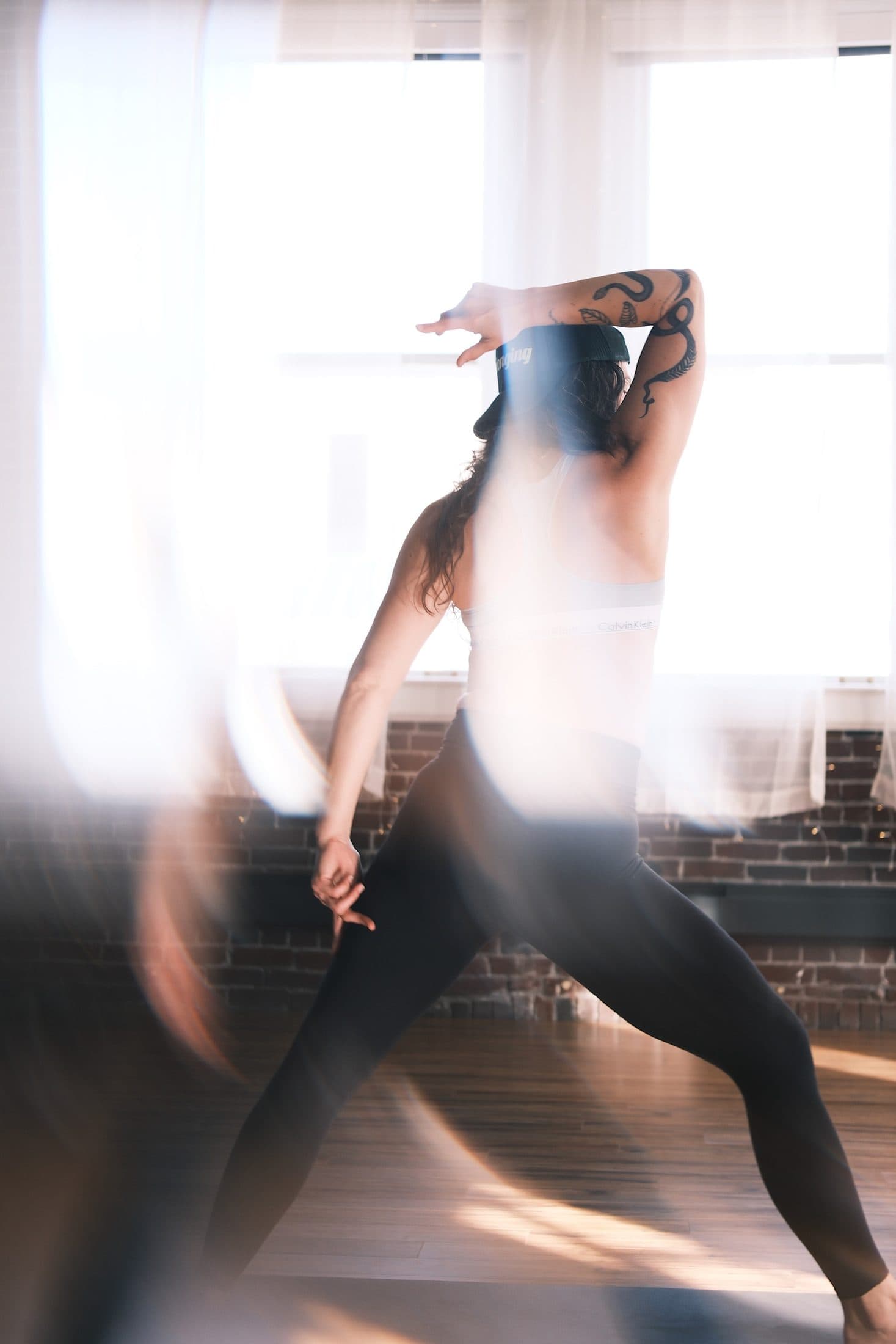 Practitioner mid-movement, arms crossing overhead, motion trails against brick and windows